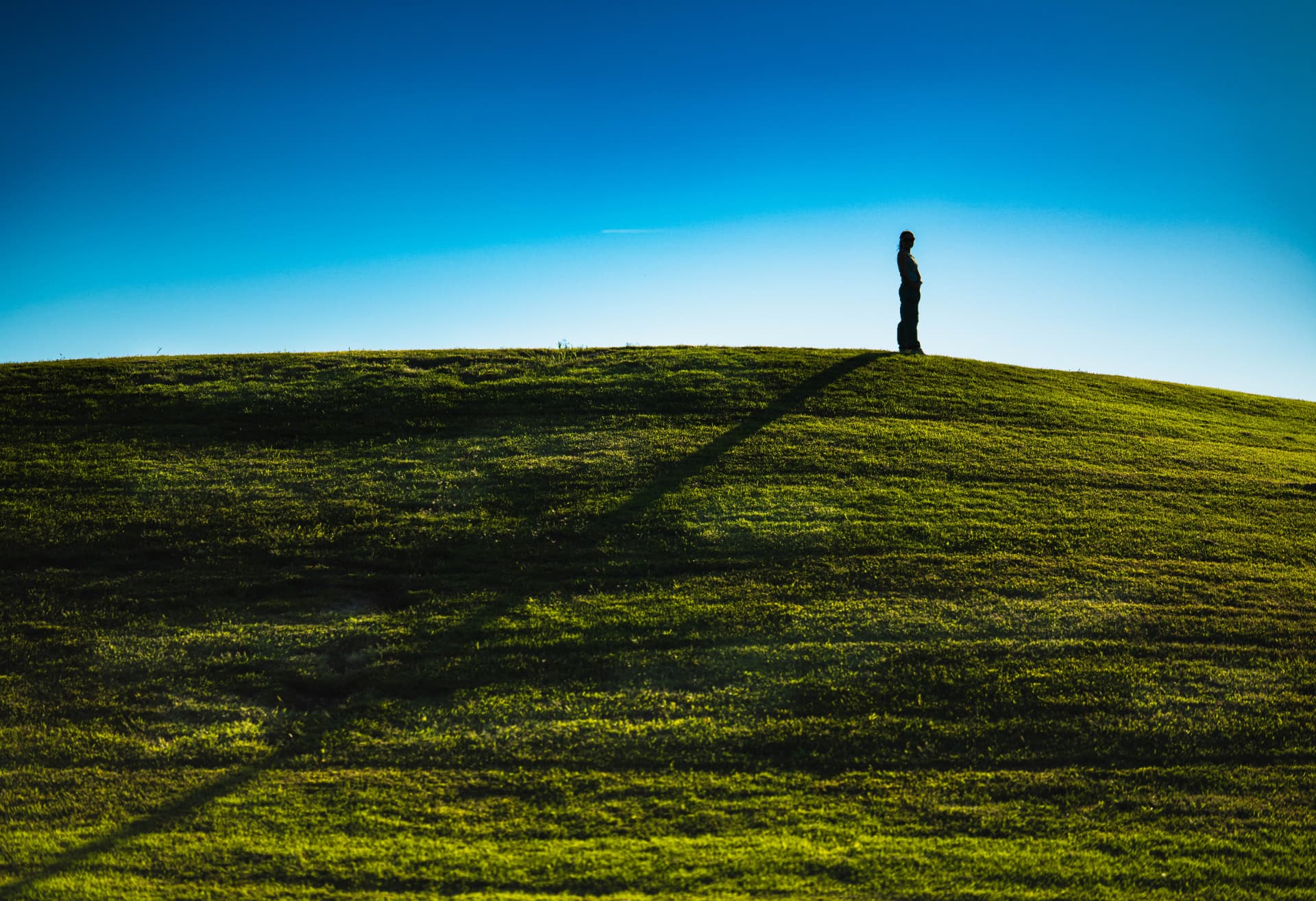 The Distance Between — a lone figure on a grassy hill beneath a wide blue sky